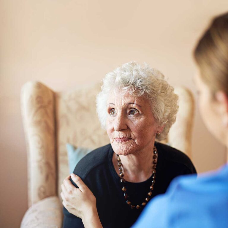 A senior unpacking a box in a cozy assisted living apartment with family assisting and caregiver nearby.